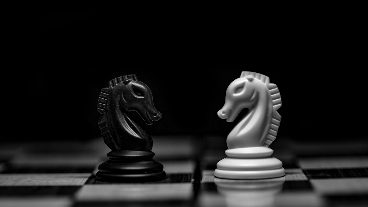 a black and a white chess knight facing each other on a board